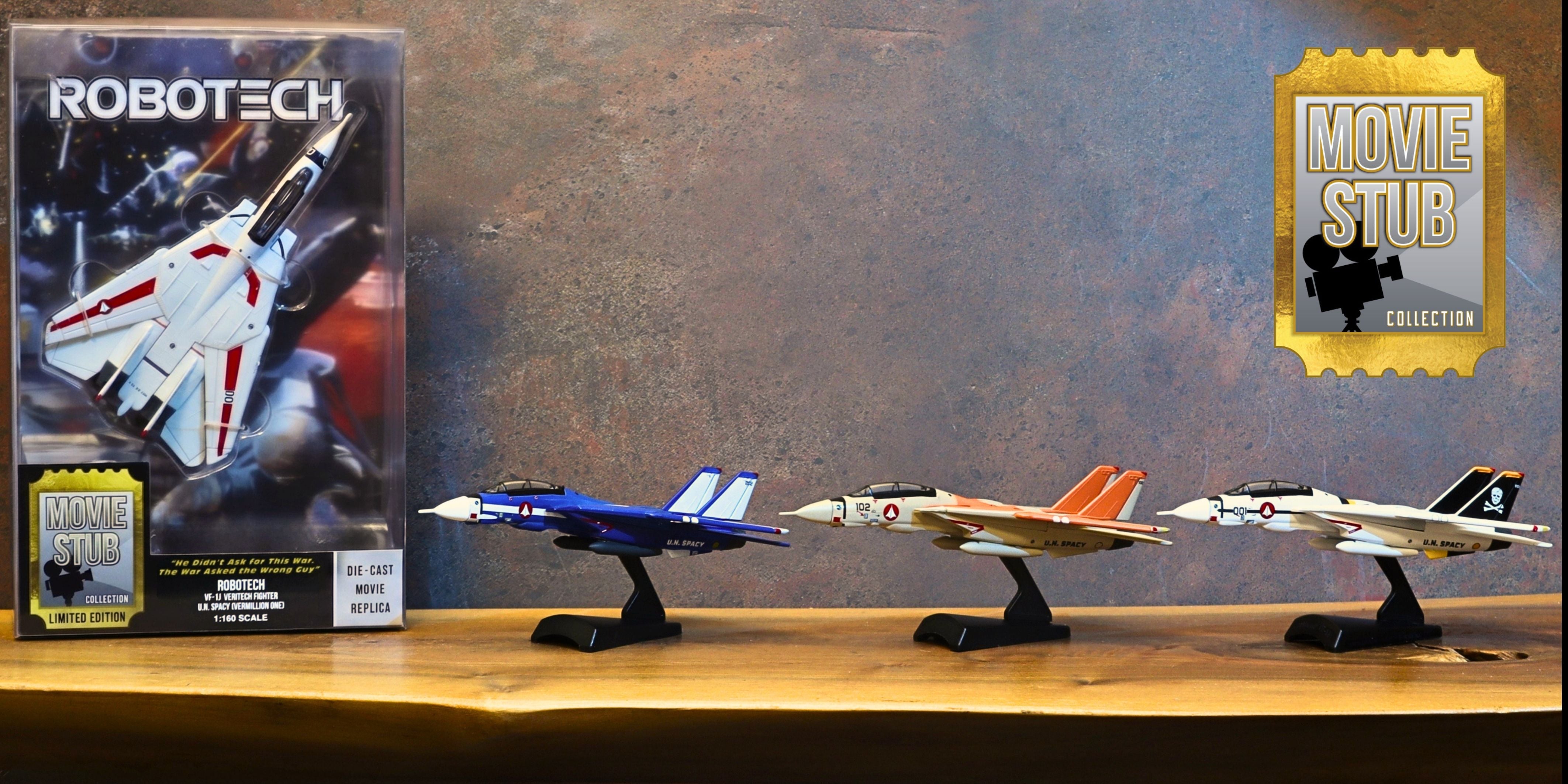 A collection of four Robotech toy fighter jets on black stands, displayed on a wooden shelf next to their original packaging box and a gold 'Movie Stub Collection' badge.