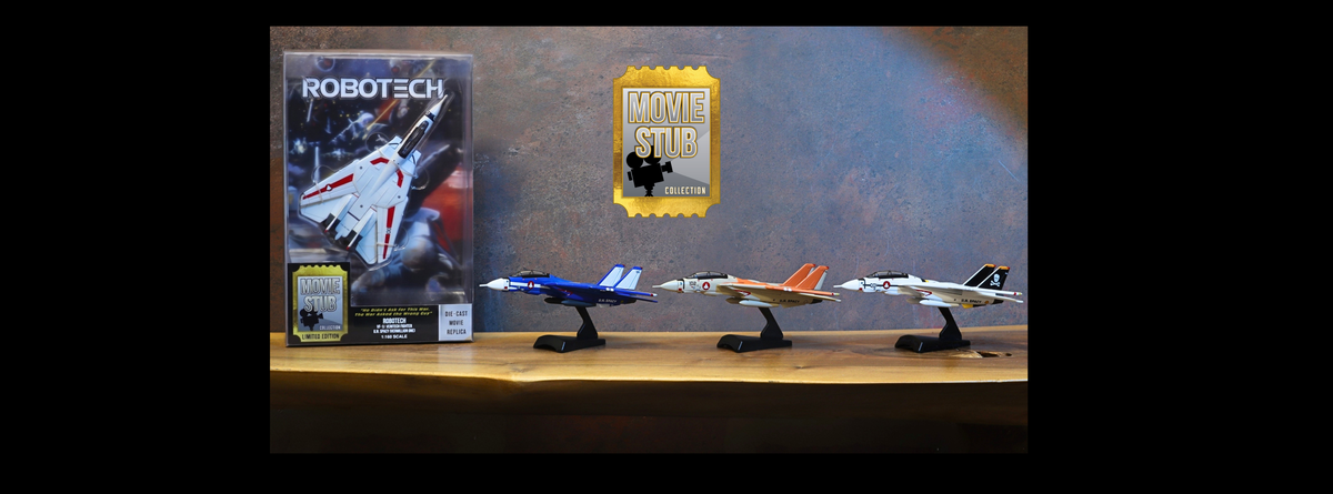 A collection of four Robotech toy fighter jets on black stands, displayed on a wooden shelf next to their original packaging box and a gold 'Movie Stub Collection' badge.